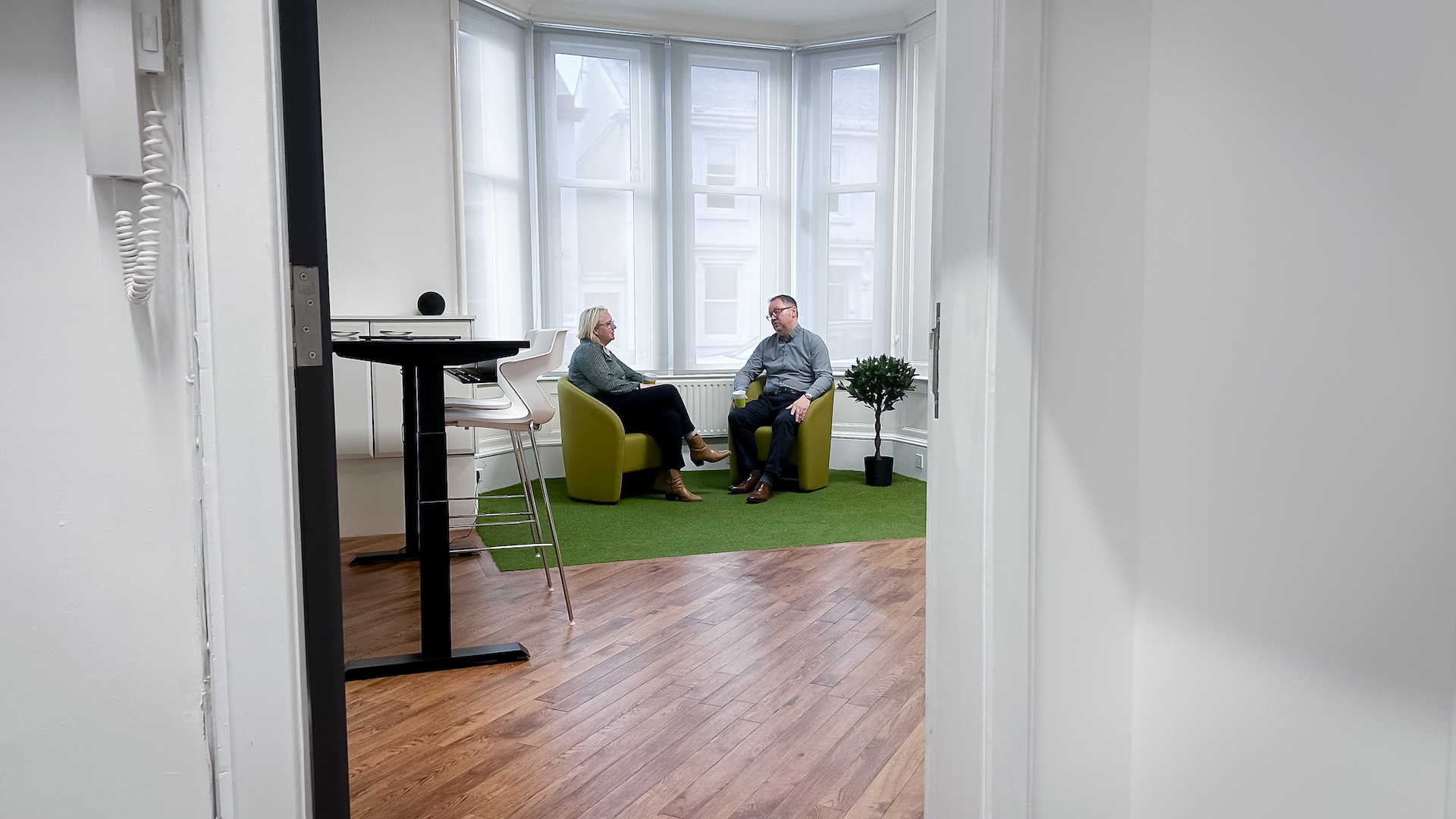 A man and woman seated on green chairs shot through a doorway